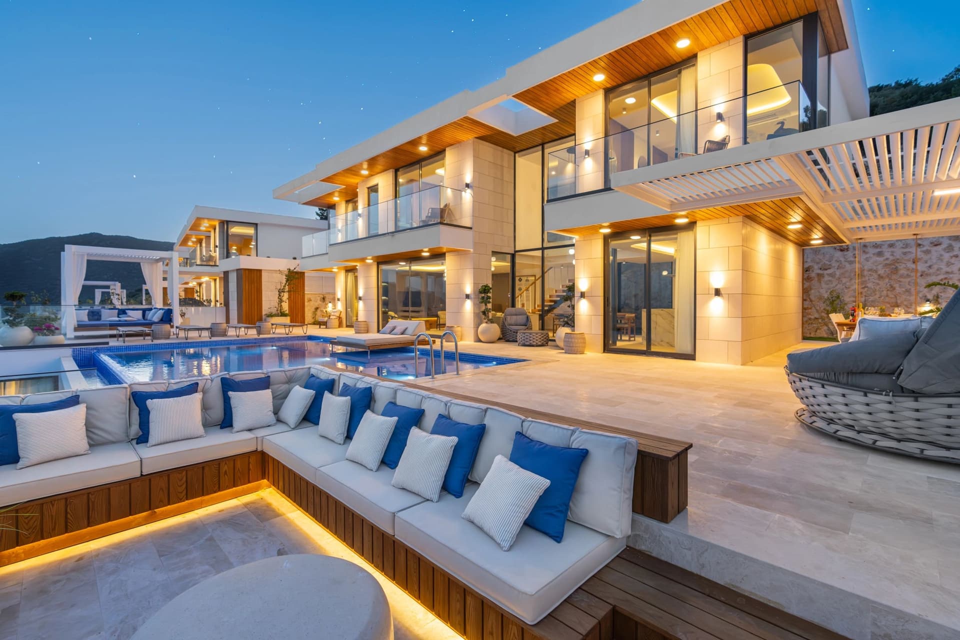 Akşam vakti havuz başı oturma grubu ve ışıklandırılmış modern villanın dış görünümü.