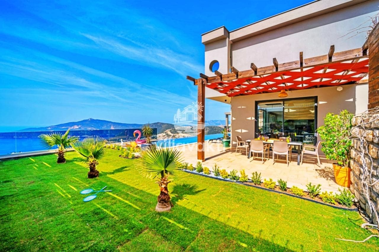 Deniz manzaralı yeşil bahçe ve çardak altındaki yemek masası.