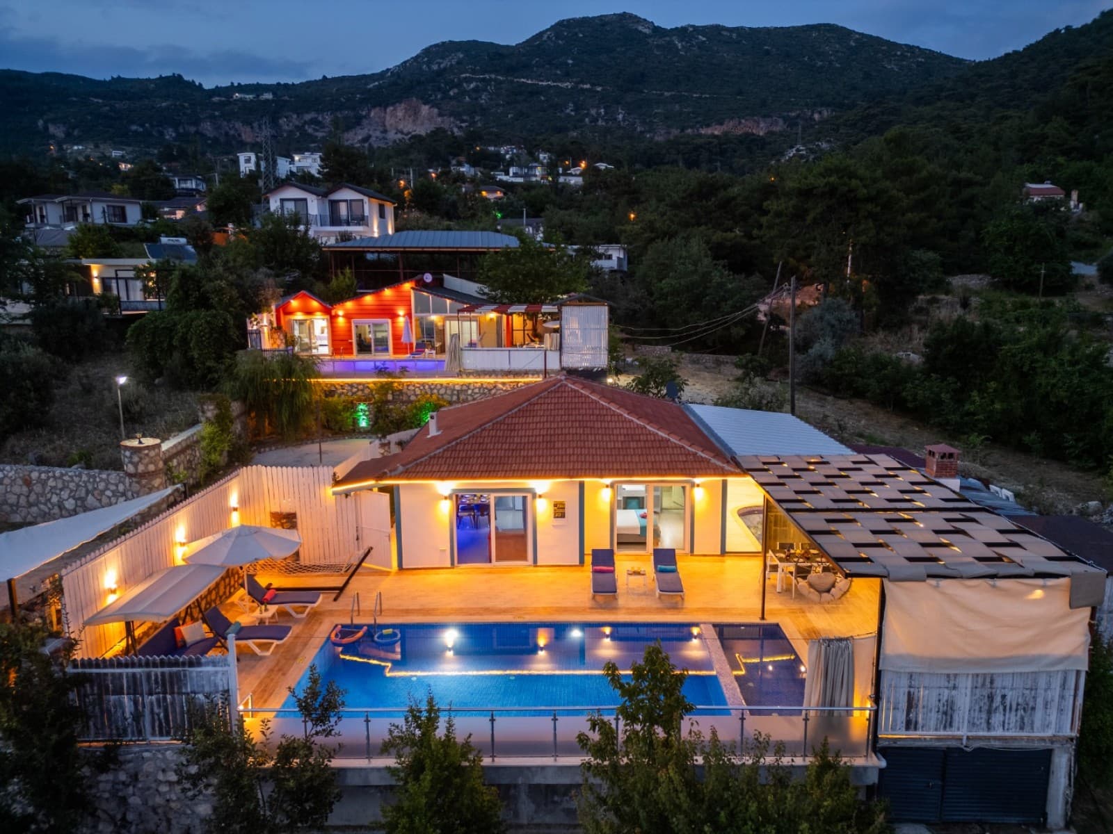 Dağ manzaralı, havuzlu tek katlı villanın akşam dış cephe görünümü.