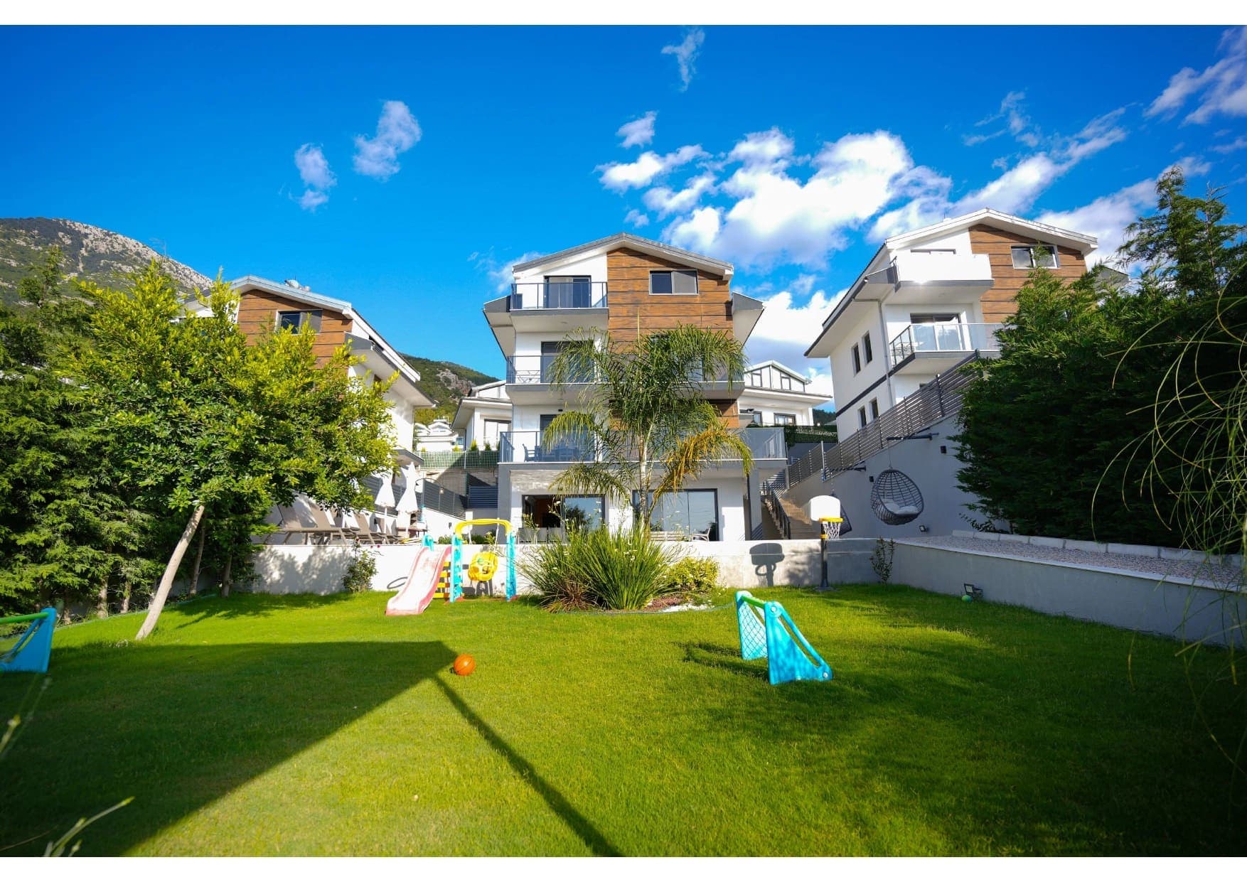 Geniş bahçesinde çocuk oyun grubu ve havuz bulunan üç katlı modern villa.