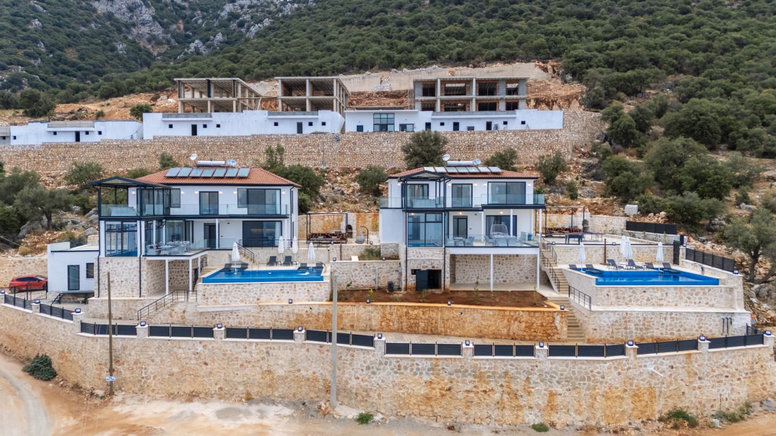Taş duvarlı iki katlı ikiz villalar ve önlerinde mavi havuzlar.