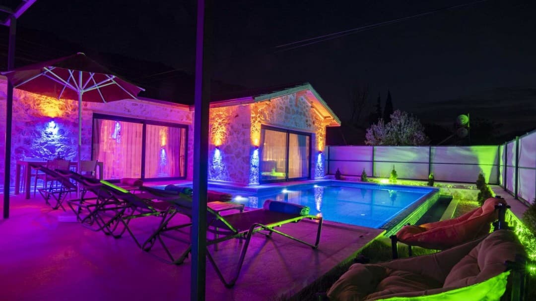 Gece aydınlatmalı taş villa, özel yüzme havuzu, şezlonglar ve bahçe mobilyaları.