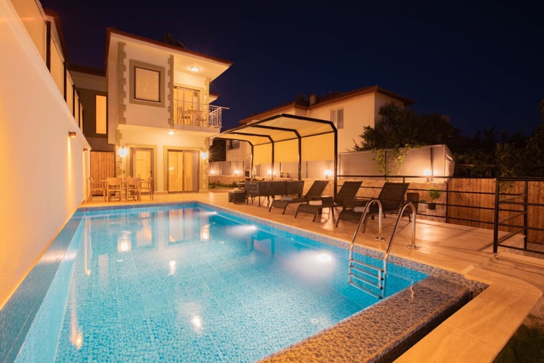Gece aydınlatmalı havuzu, şezlongları ve gölgelikli oturma alanı bulunan iki katlı müstakil villa.