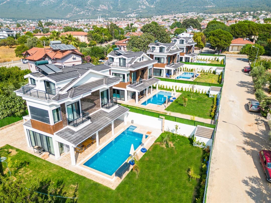 Havuzlu lüks villalar, çim bahçe ve arka planda yerleşim yeri ile dağ manzarası.