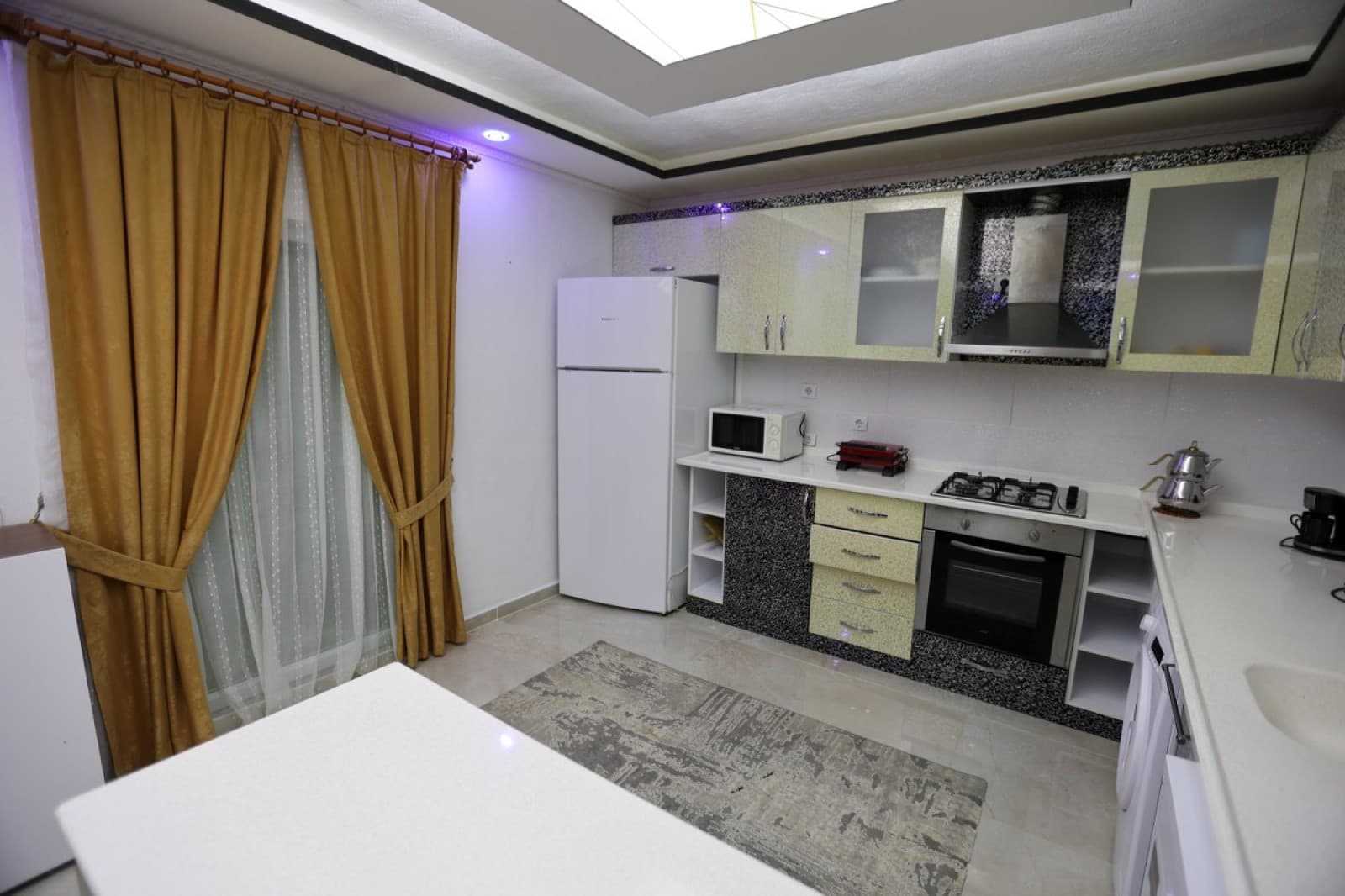 Sarı tonlarında dolaplar ve beyaz tezgahlı mutfak alanı.