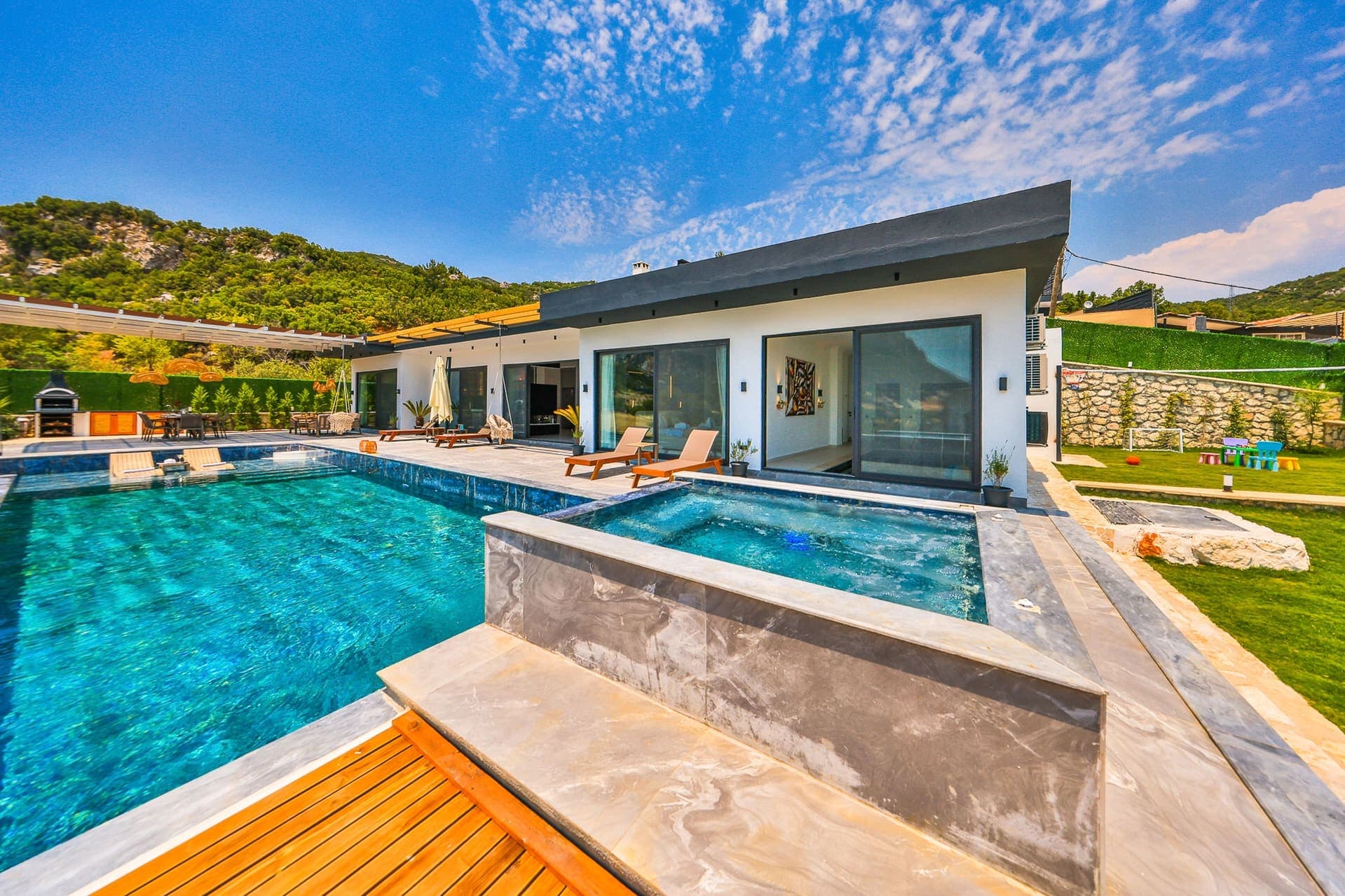 Villa dış cephesinde yüzme havuzu, jakuzi ve şezlonglar bulunuyor.