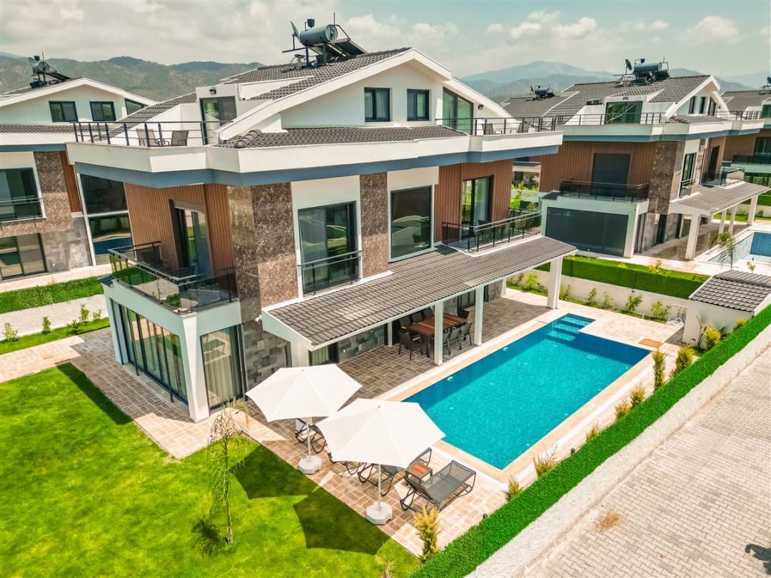 Önünde özel havuzu, şezlongları ve güneş şemsiyeleri bulunan üç katlı modern villa.
