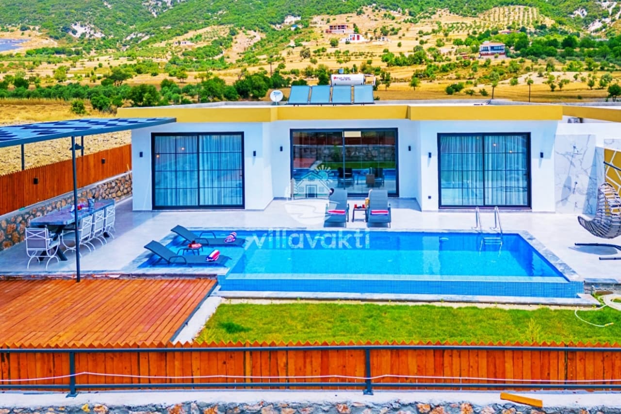 Tek katlı beyaz villanın önünde havuz, şezlonglar ve dağ manzarası yer alıyor.