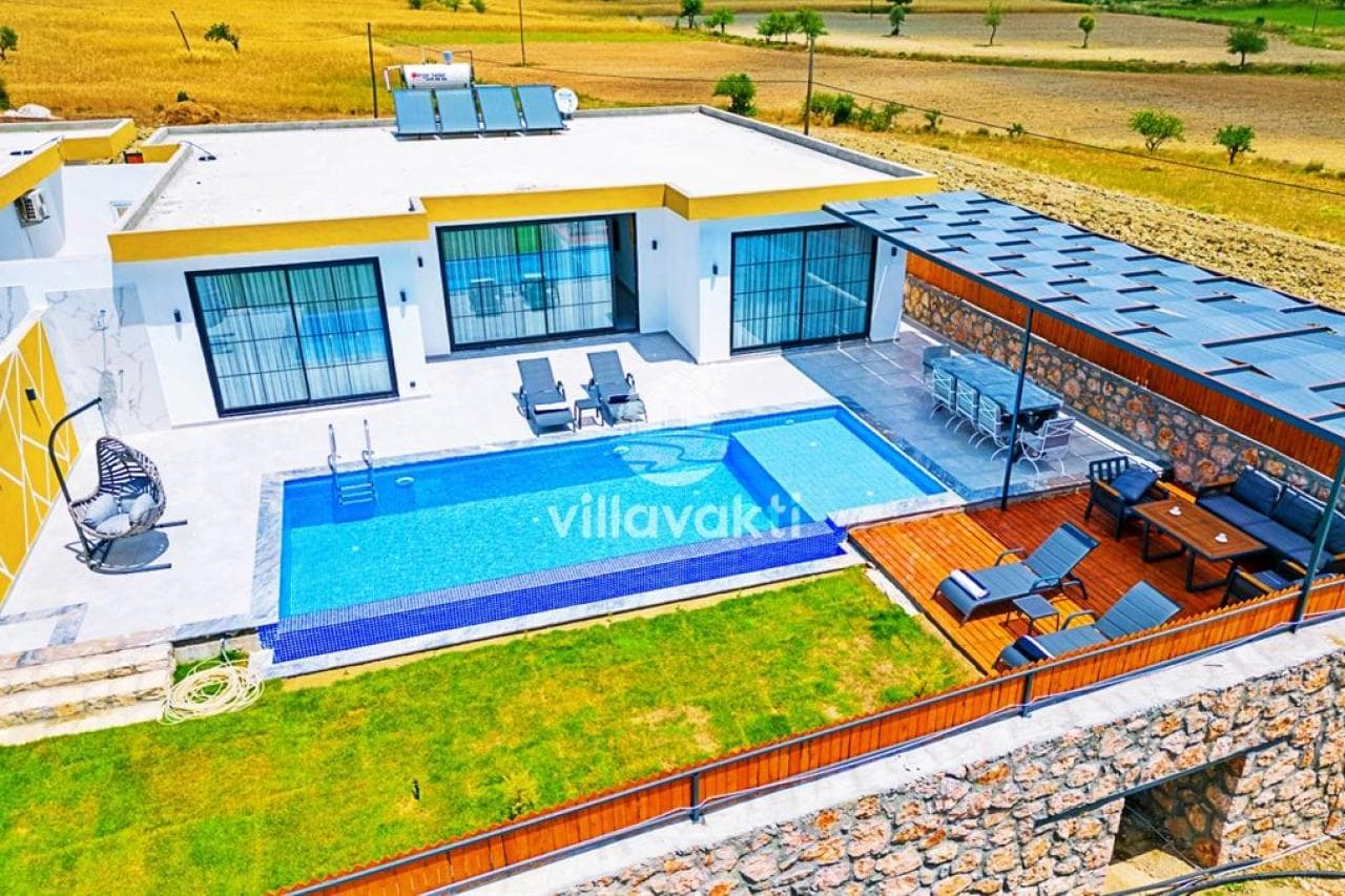 Havuzlu villa ve bahçesindeki şezlonglar ile yemek masası.