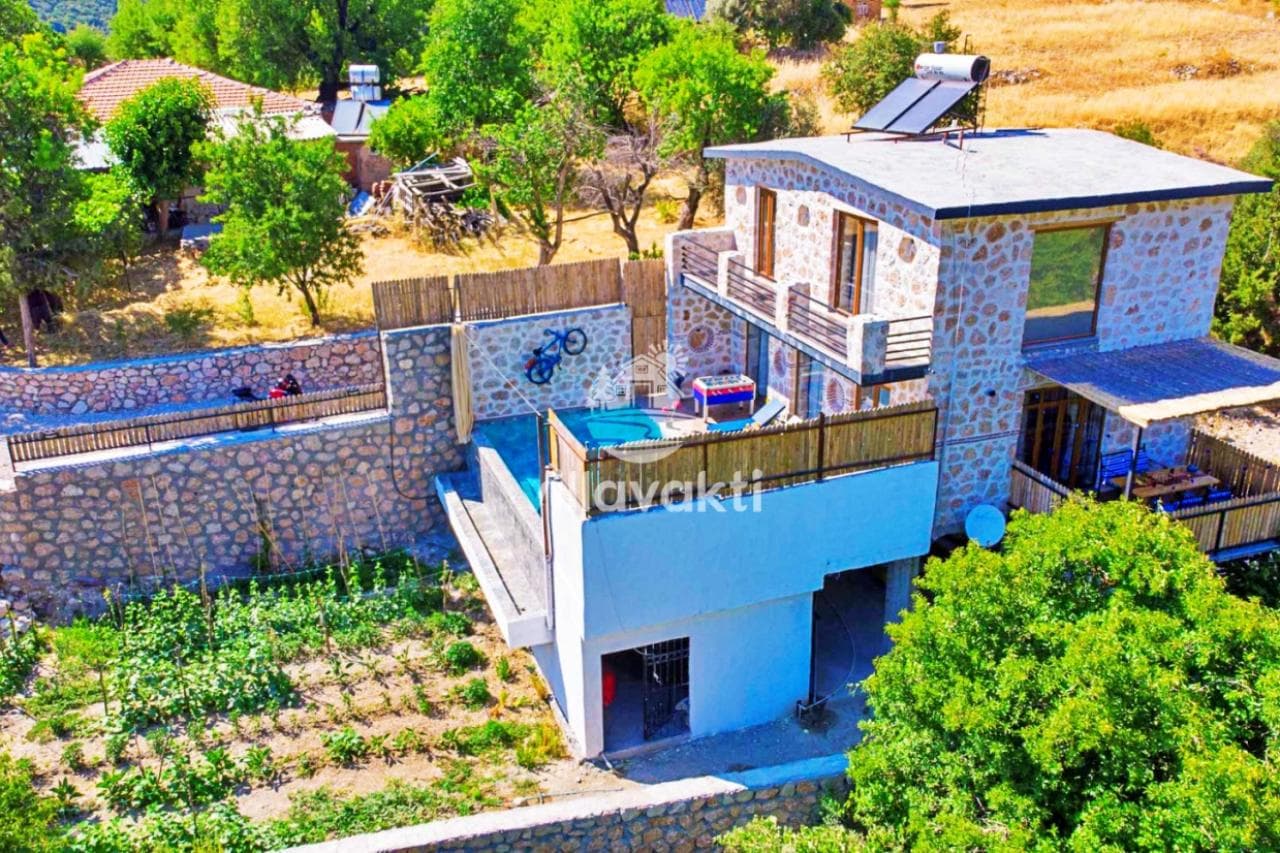 Taş kaplamalı iki katlı villanın havuzlu terası ve bahçesi havadan görünüyor.