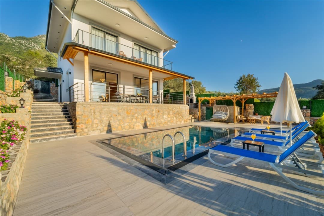 Taş kaplama duvarlı, havuzlu ve şezlonglu bahçeye sahip iki katlı müstakil villa.