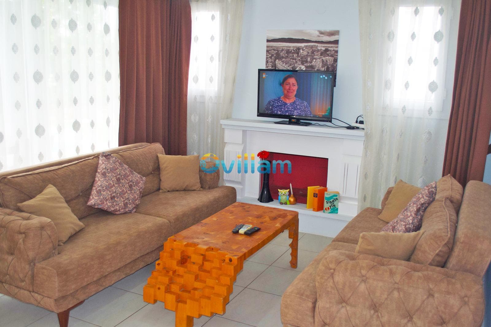 Kahverengi koltuklar, ahşap orta sehpa ve beyaz TV ünitesine sahip iç mekân.