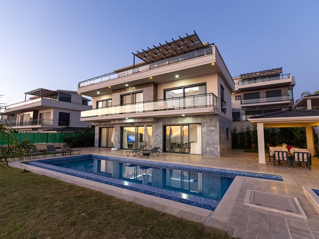 Akşam vakti aydınlatılmış, özel havuzlu ve teraslı modern üç katlı villa.