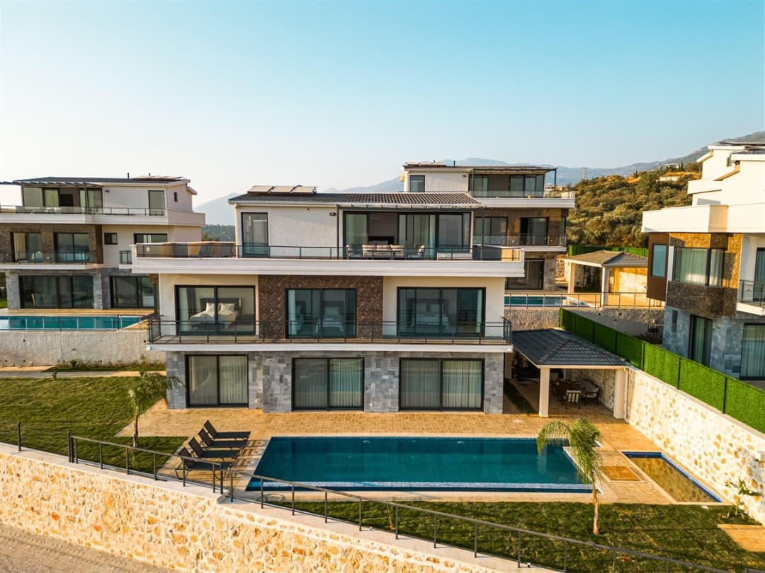 Gündüz vakti geniş bahçesi, havuzu ve balkonları olan modern çok katlı villa dış cephesi.