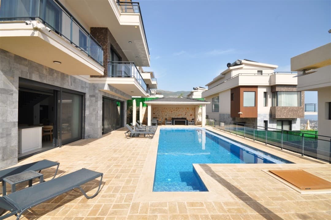 Villa cephesi önünde uzun havuz ve taş döşeli teras.