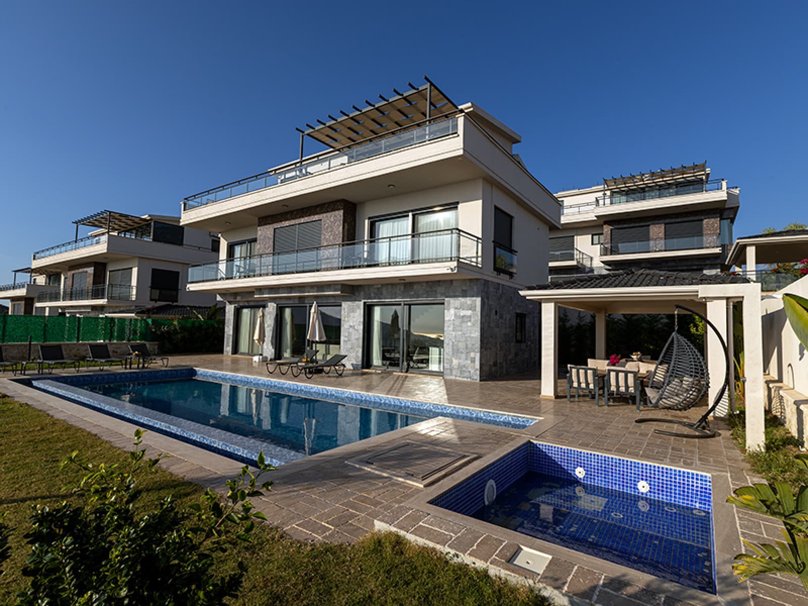 Önünde yüzme havuzu ve şezlonglar bulunan modern villa dış cephesi.