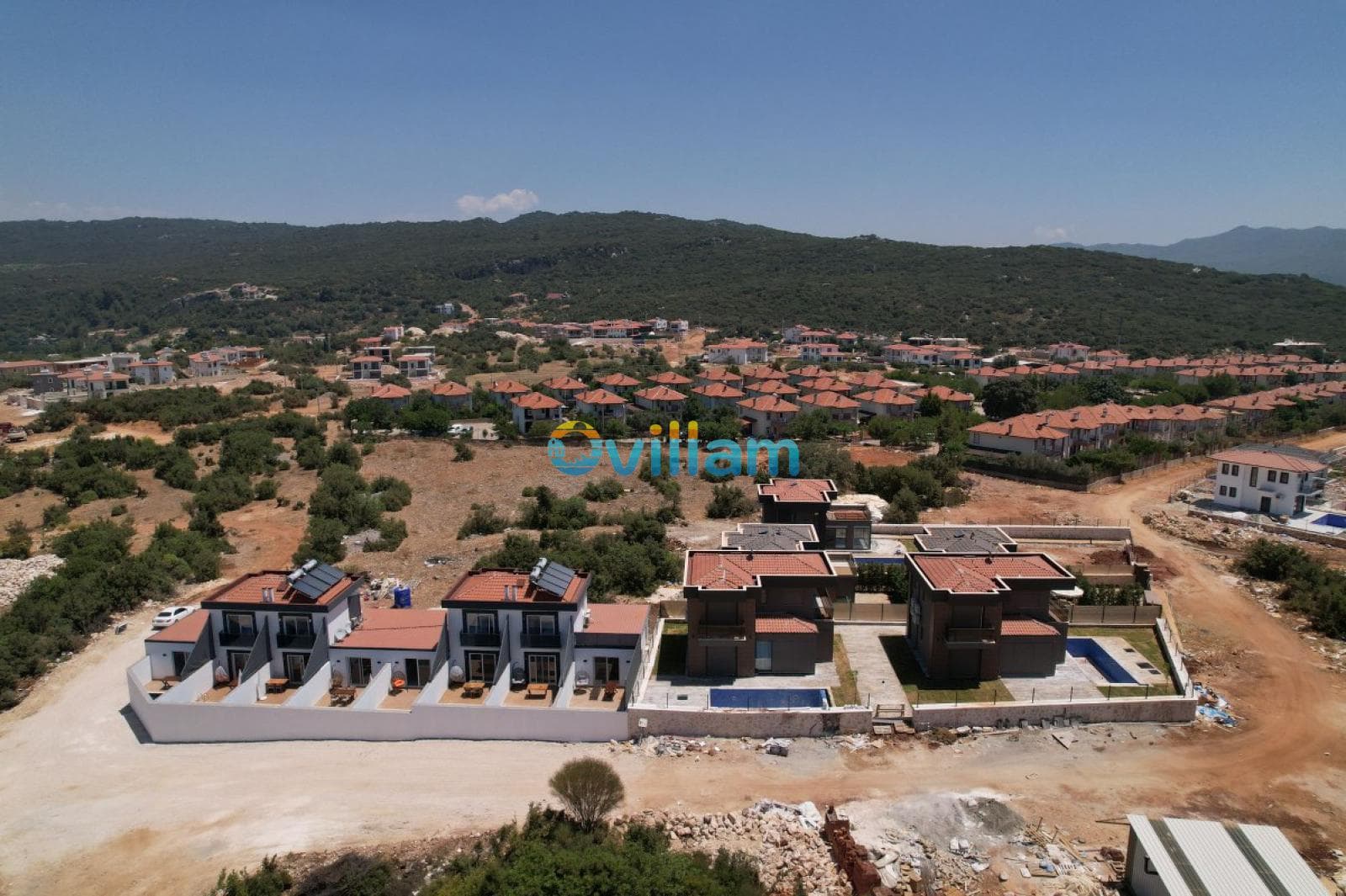 Kiremit çatıları olan villaların bulunduğu yerleşimin havadan görünümü.