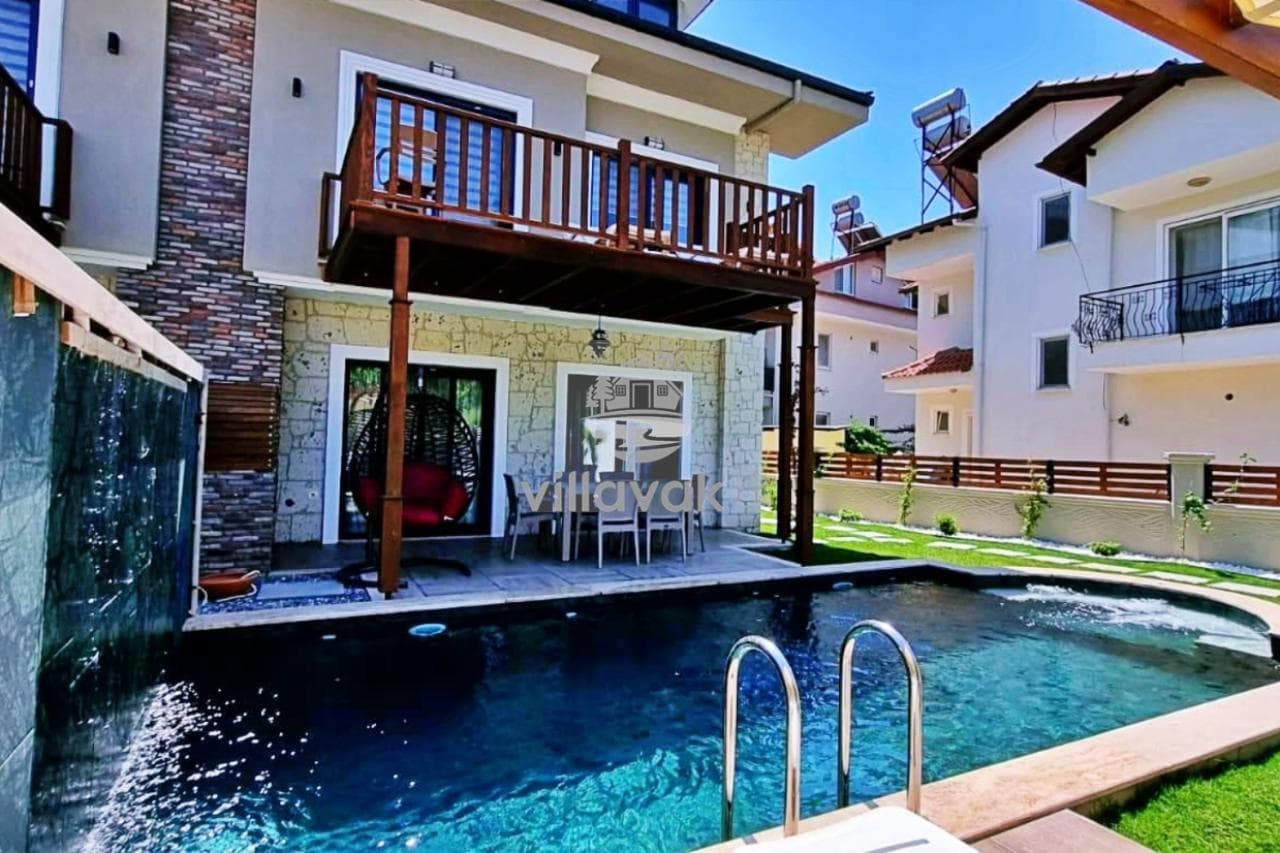 Mavi havuzlu, ahşap balkonlu ve bahçe oturma grubuna sahip taş detaylı villa.