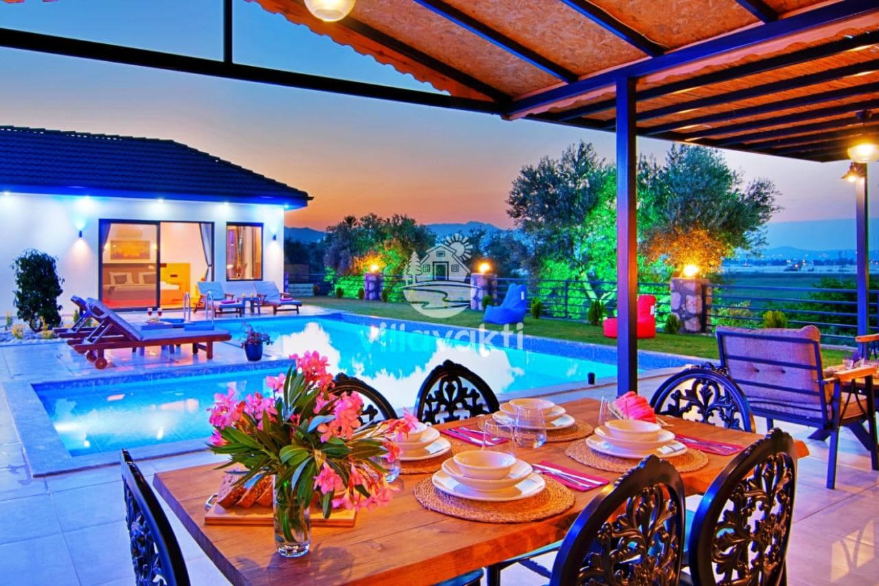 Akşam vakti havuz başındaki yemek masası ve villanın dış görünümü.