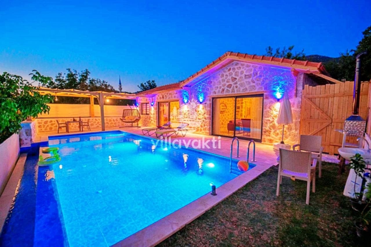 Akşam vakti aydınlatmalı taş villanın havuzu ve bahçe oturma alanı