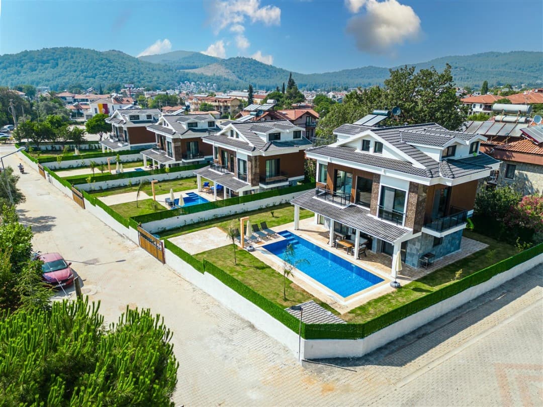 Gündüz vakti havuzlu ve bahçeli yan yana sıralı iki katlı villaların havadan görünümü.