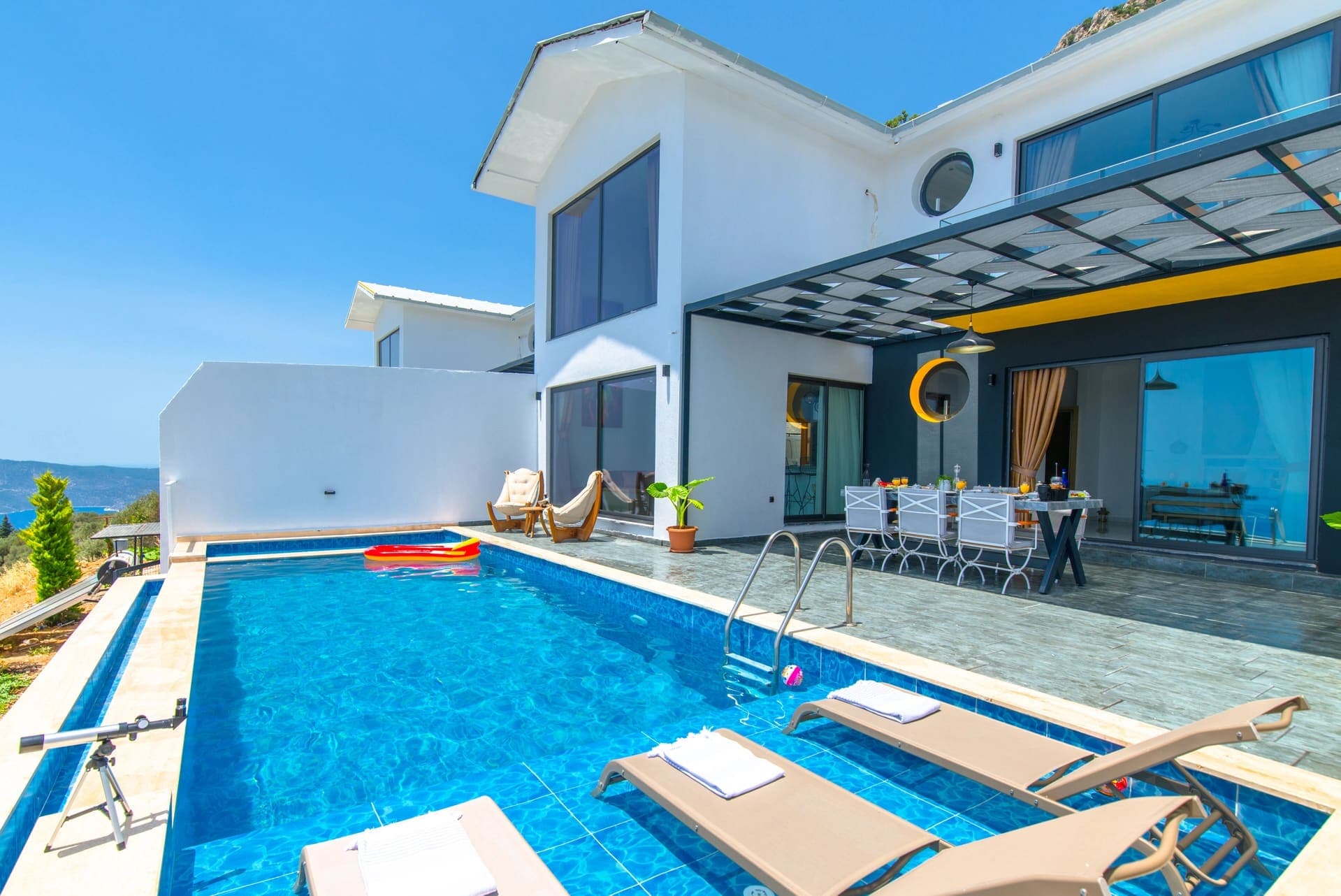 Havuz kenarında şezlonglar ve beyaz dış cepheli villa.