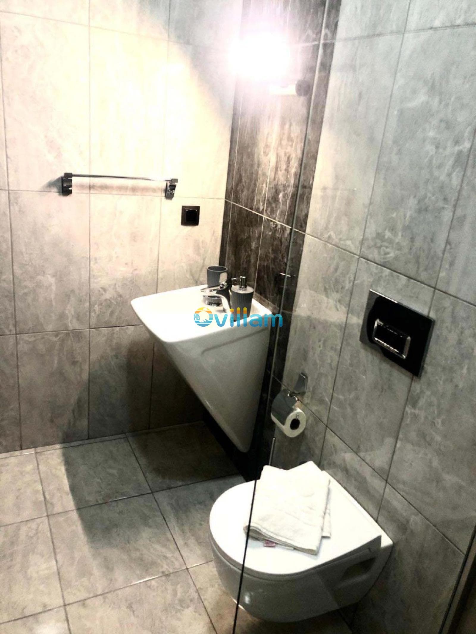 Gri tonlarında mermer kaplı banyoda beyaz lavabo ve asma klozet.