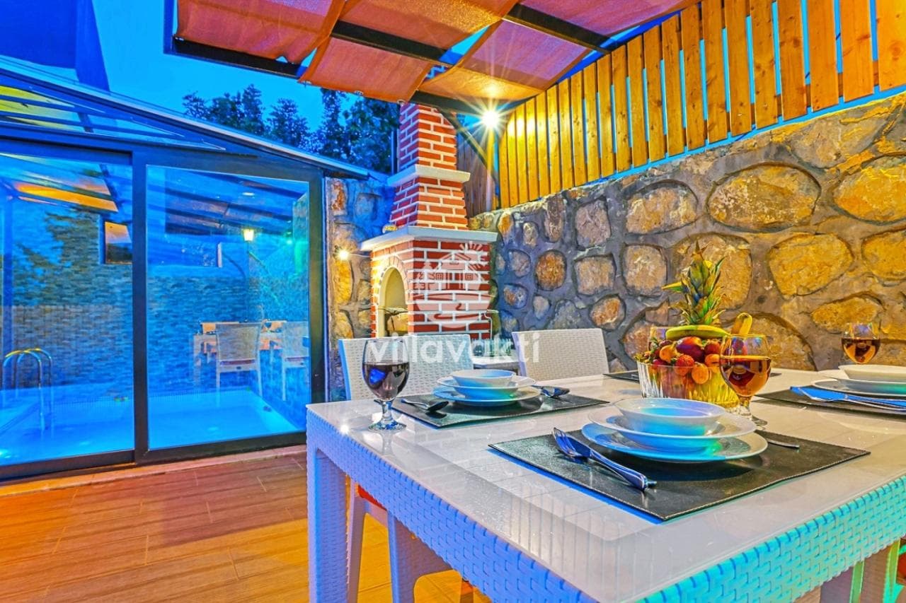 Verandada şömineli yemek masası ve havuz manzarası.