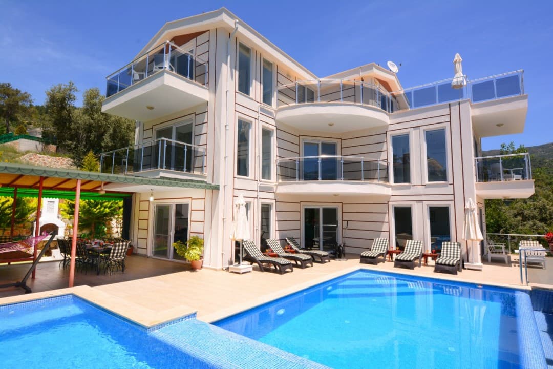 Gündüz vakti havuz başı şezlongları ve balkonları olan iki katlı lüks bir villa.