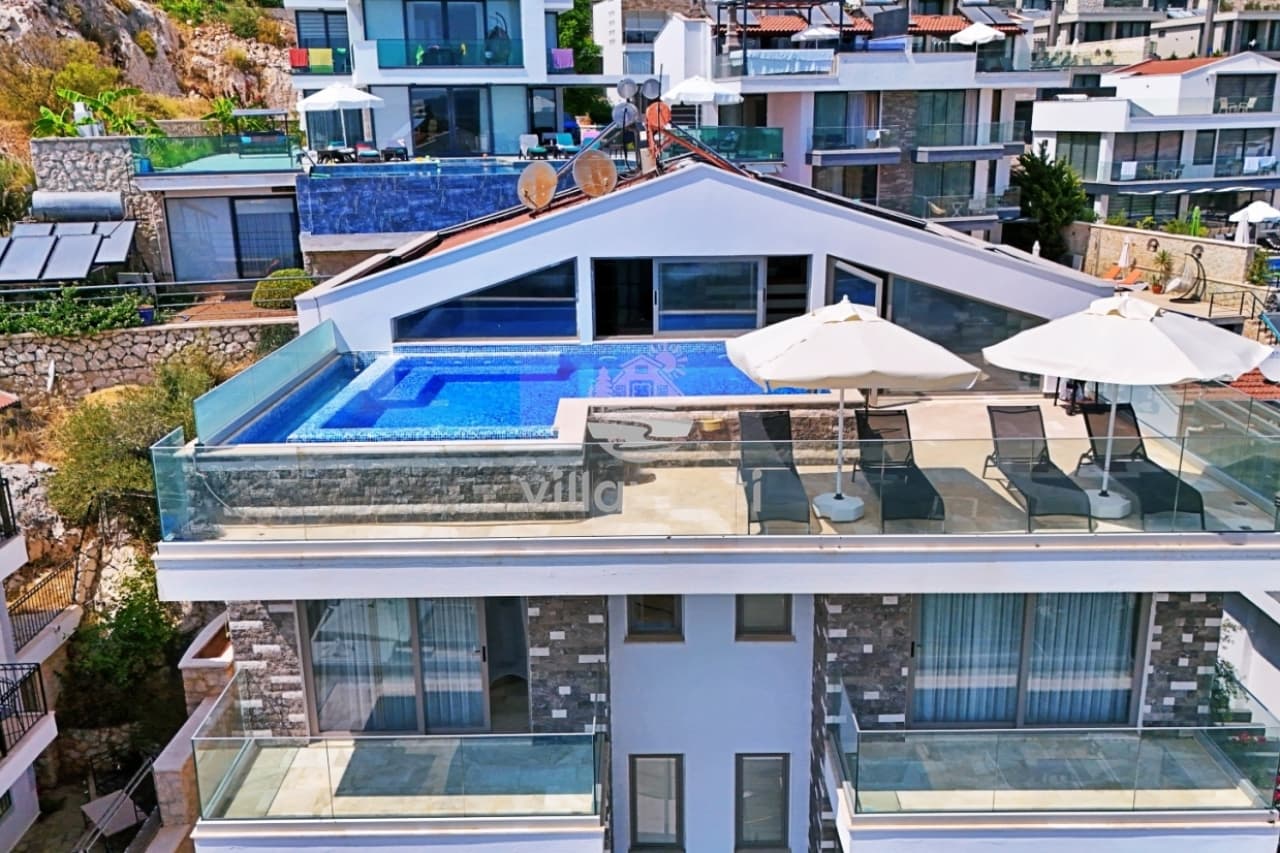 Teras katında yüzme havuzu ve şezlonglar bulunan, balkonlu modern villanın dış cephesi.