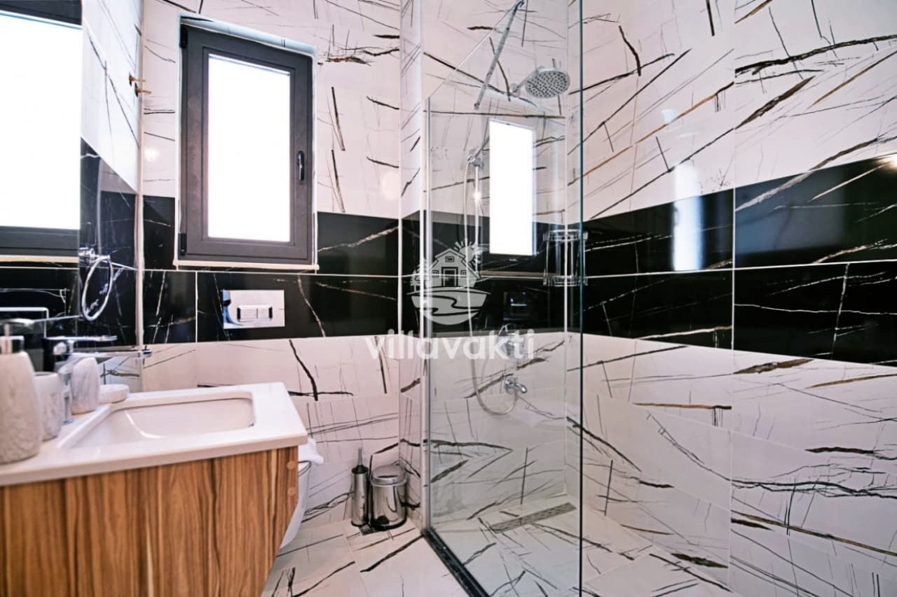 Siyah beyaz damarlı mermer duvar kaplamalarına sahip duş alanı ve lavabo.