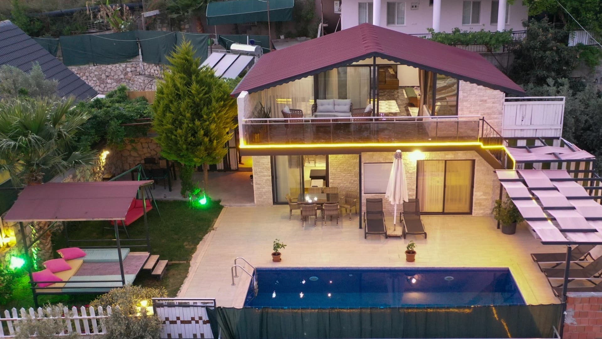 Akşam aydınlatmalı, havuzlu, balkonlu ve bahçesinde oturma alanı bulunan iki katlı taş villa.