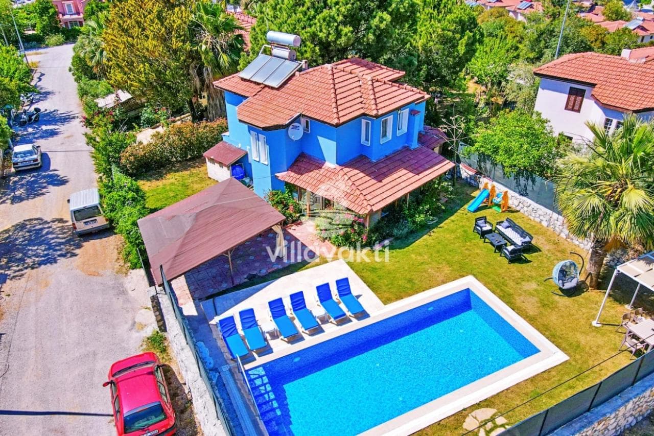 Mavi cepheli villanın havuzu ve şezlonglarla döşenmiş bahçesi.
