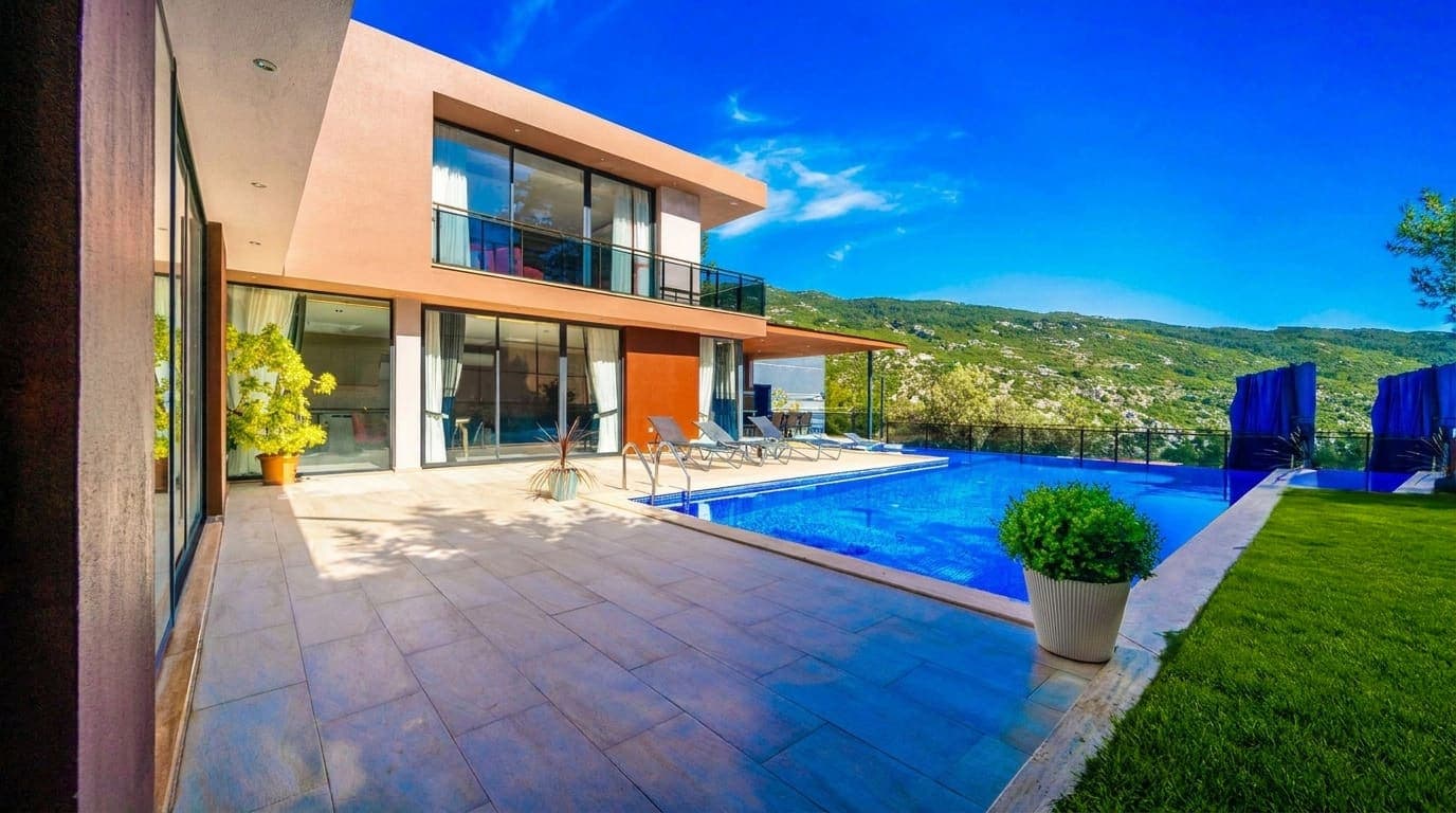 Geniş cam cepheli modern villanın önünde havuz ve güneşlenme terası var.