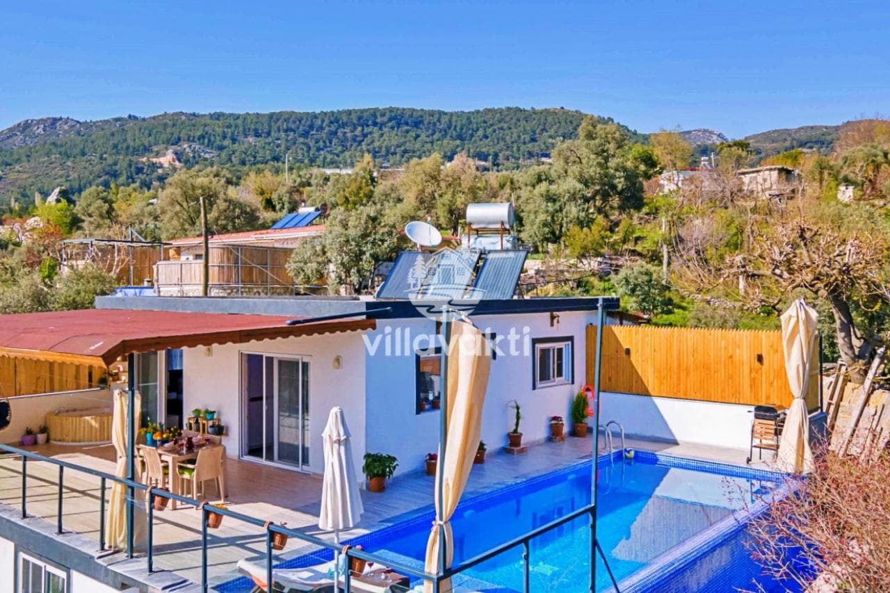 Önünde açık havuz ve şezlonglar bulunan, dağ manzaralı tek katlı villa dış cephesi.