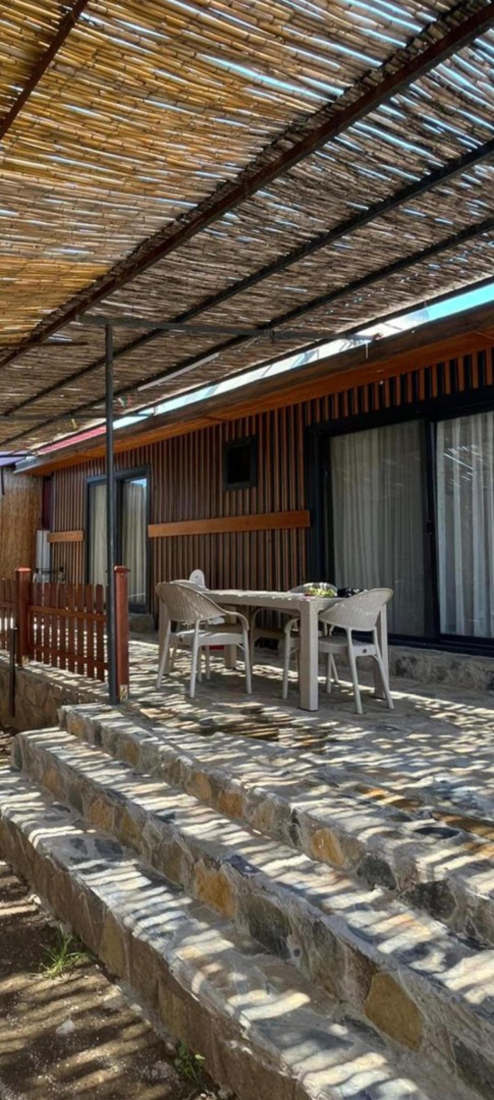 Hasır gölgelikli, taş basamaklı veranda alanında masa ve sandalyeler.