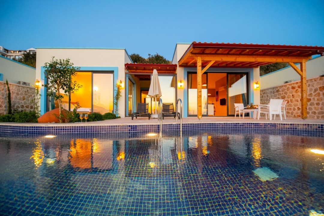 Akşamüstü aydınlatmalı havuzun arkasında yer alan tek katlı villa.