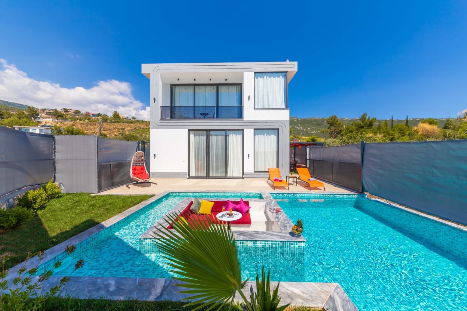 Bahçesinde havuz ve havuz içinde oturma alanı bulunan modern iki katlı villa dış cephesi.