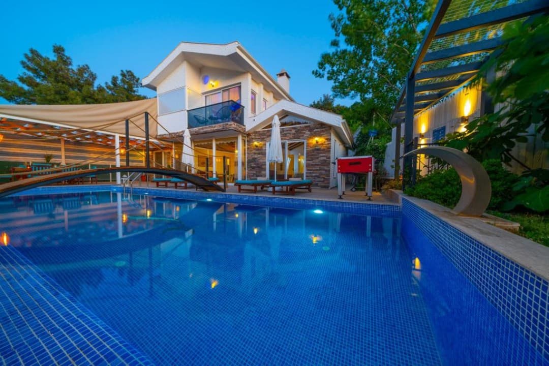 Akşam karanlığında havuz ve şezlongları bulunan iki katlı villa.
