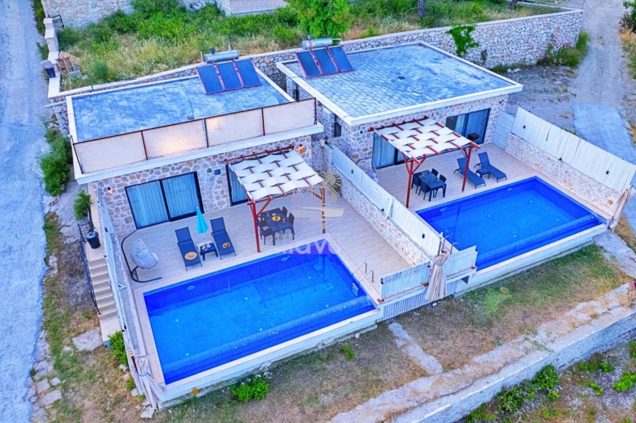 Özel havuzları ve şezlong alanları olan taş villa ikilisinin havadan görünümü.