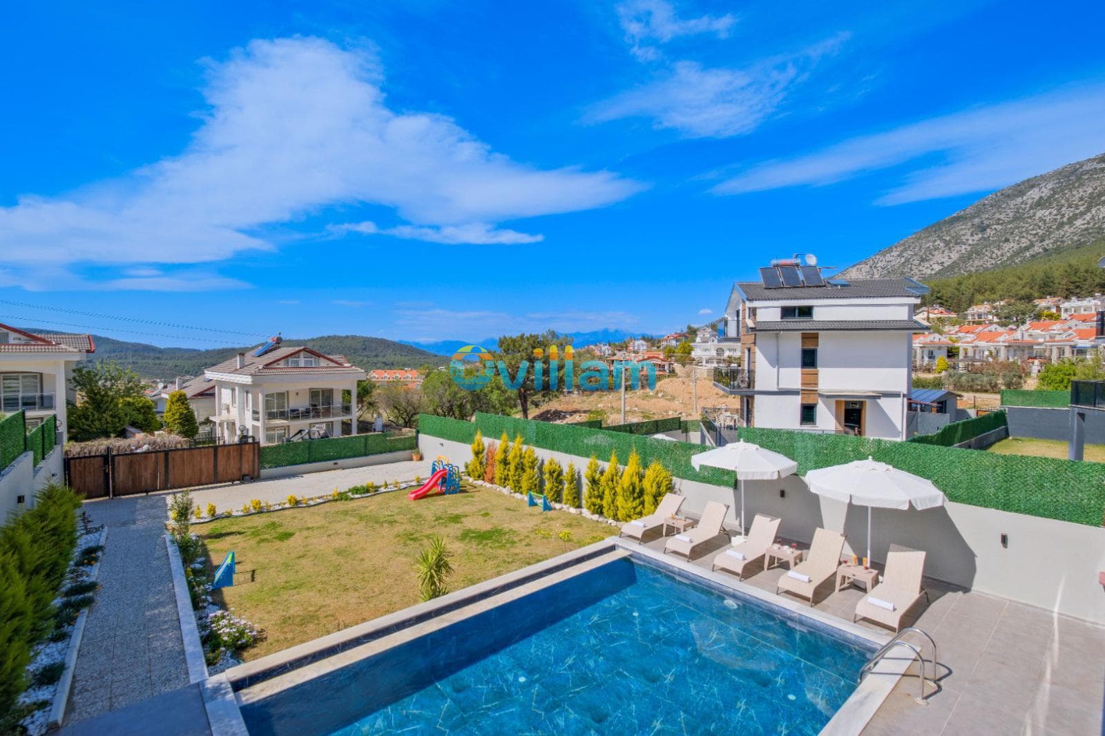 Yeşil çim alanlı bahçesi, havuzu ve şezlongları olan iki katlı villa.