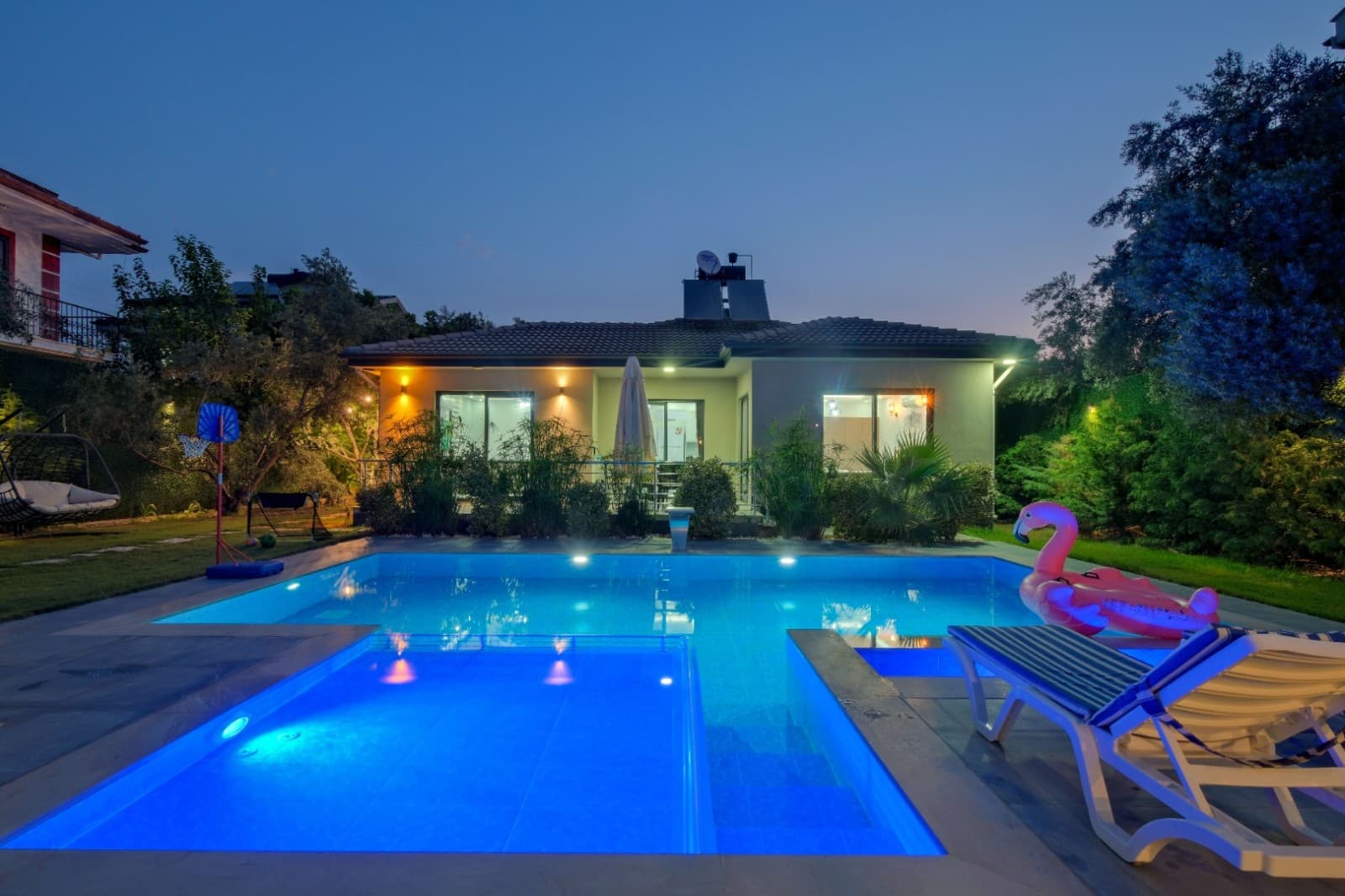 Aydınlatmalı havuz ve pembe flamingo deniz yatağı olan villa bahçesi.