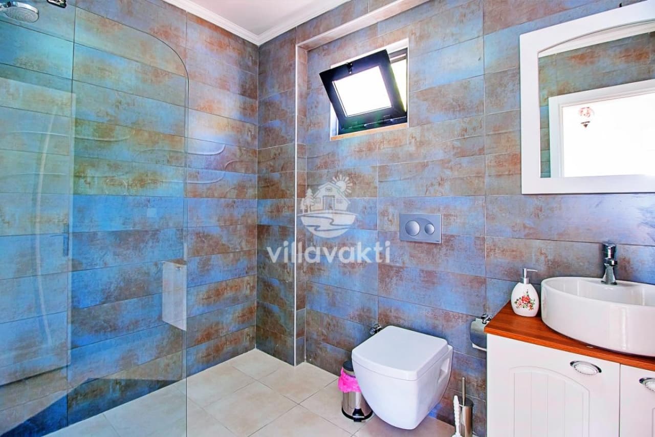 Cam duş kabini, tezgah üstü lavabo ve klozet bulunan modern banyo.
