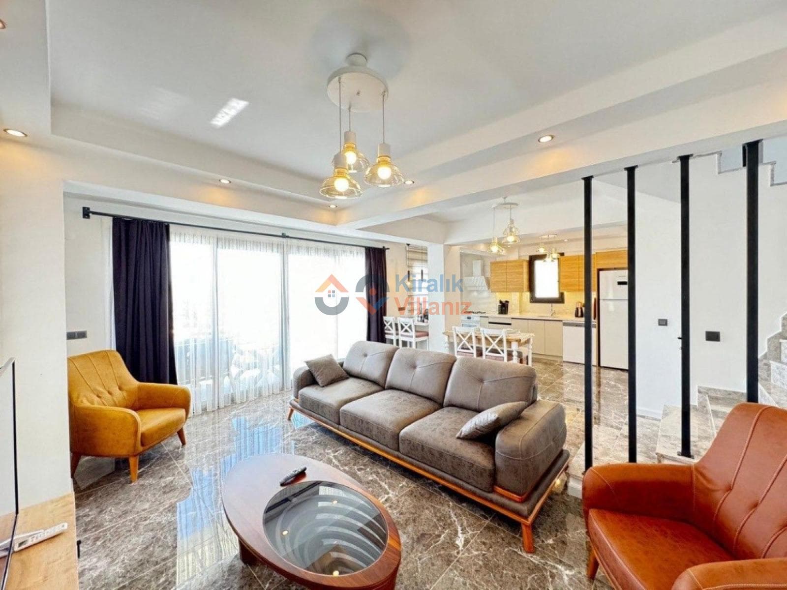 Modern salon içerisinde gri koltuk takımı, hardal sarısı tekli koltuk, orta sehpa ve mutfak bulunur.