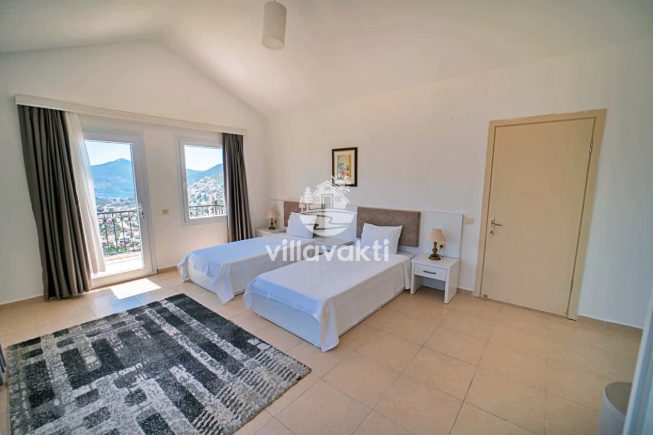 İki tek kişilik yatak, desenli halı ve balkon kapısı bulunan aydınlık yatak odası.