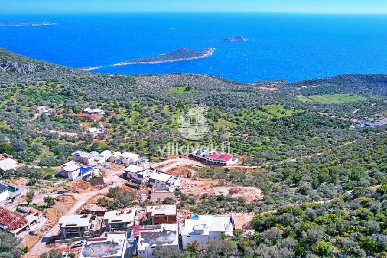 Ağaçlık alanın ortasında yer alan villalara ve uzaktaki denize bakan yüksek açı manzarası.