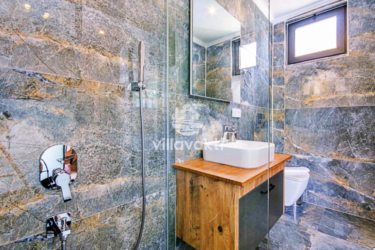 Yeşil ve kahverengi tonlarında mermer kaplı duş alanı ve lavabo.