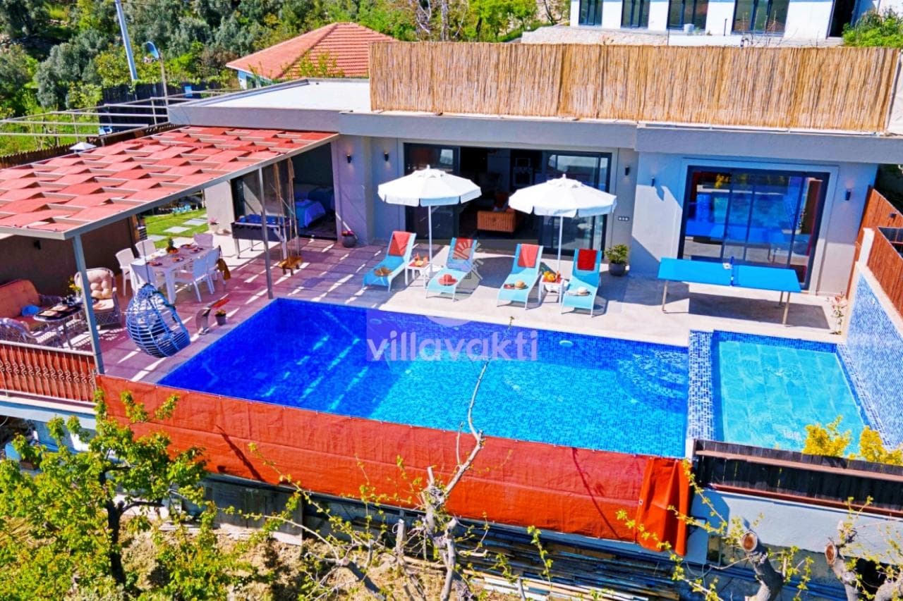 Havuz başında şezlonglar, masa ve dağ manzarası olan villa bahçesi.